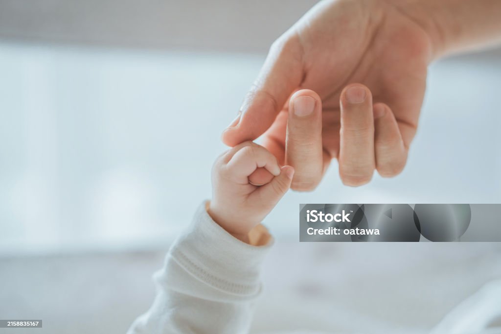 Close-up little hand of child baby holding hand of mother, A newborn holds on to mom's, dad's finger, Love and relationship with infant, Care and support, Dreaming and protection